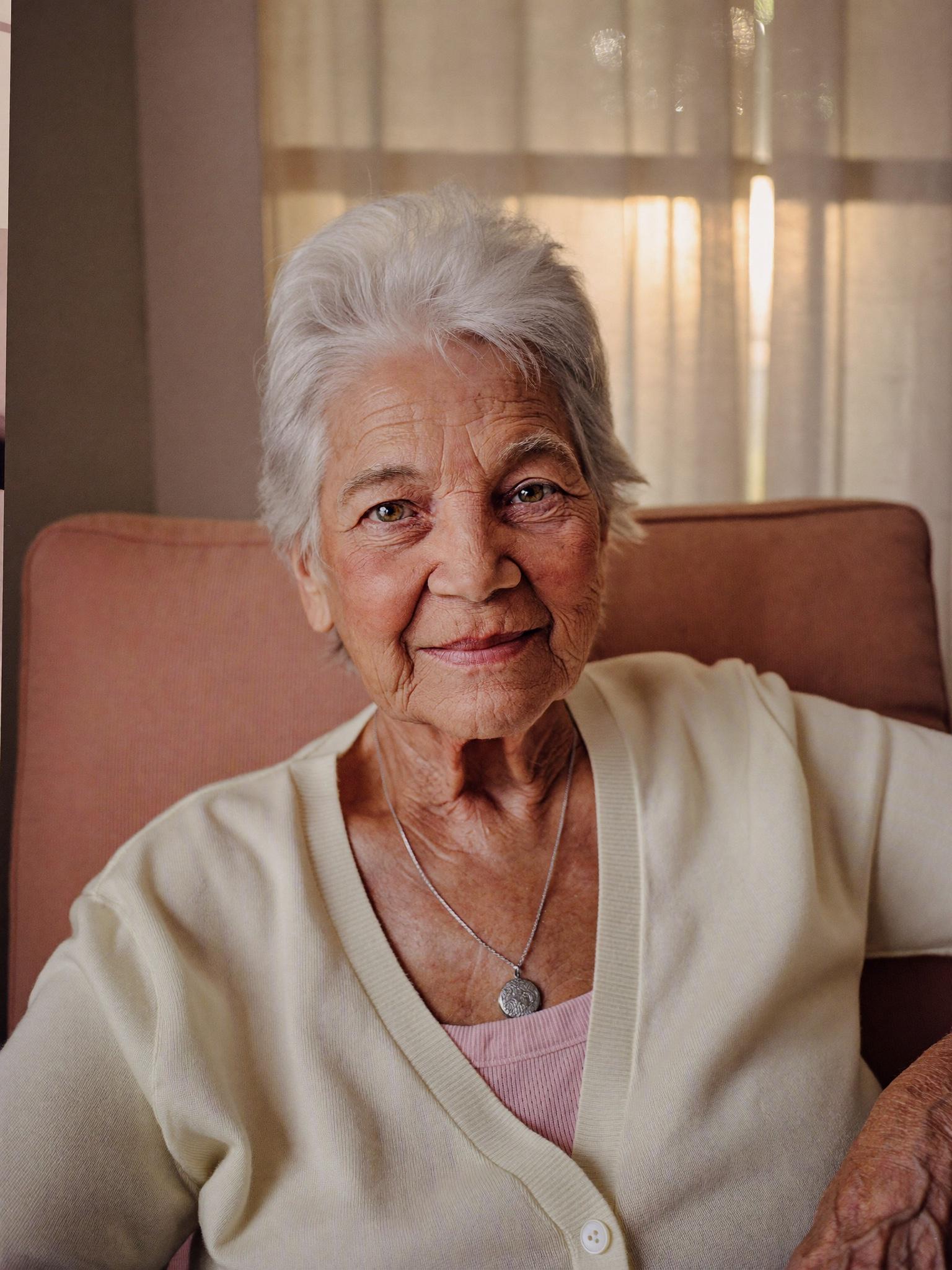 A woman in her late seventies seated in an armchair in a sunlit Florida home.