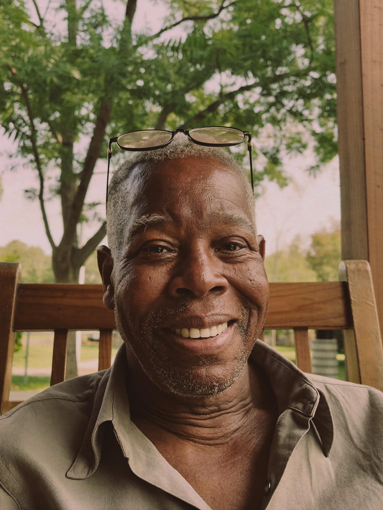 A Black man in his late sixties on a wooden porch in an Atlanta neighborhood.