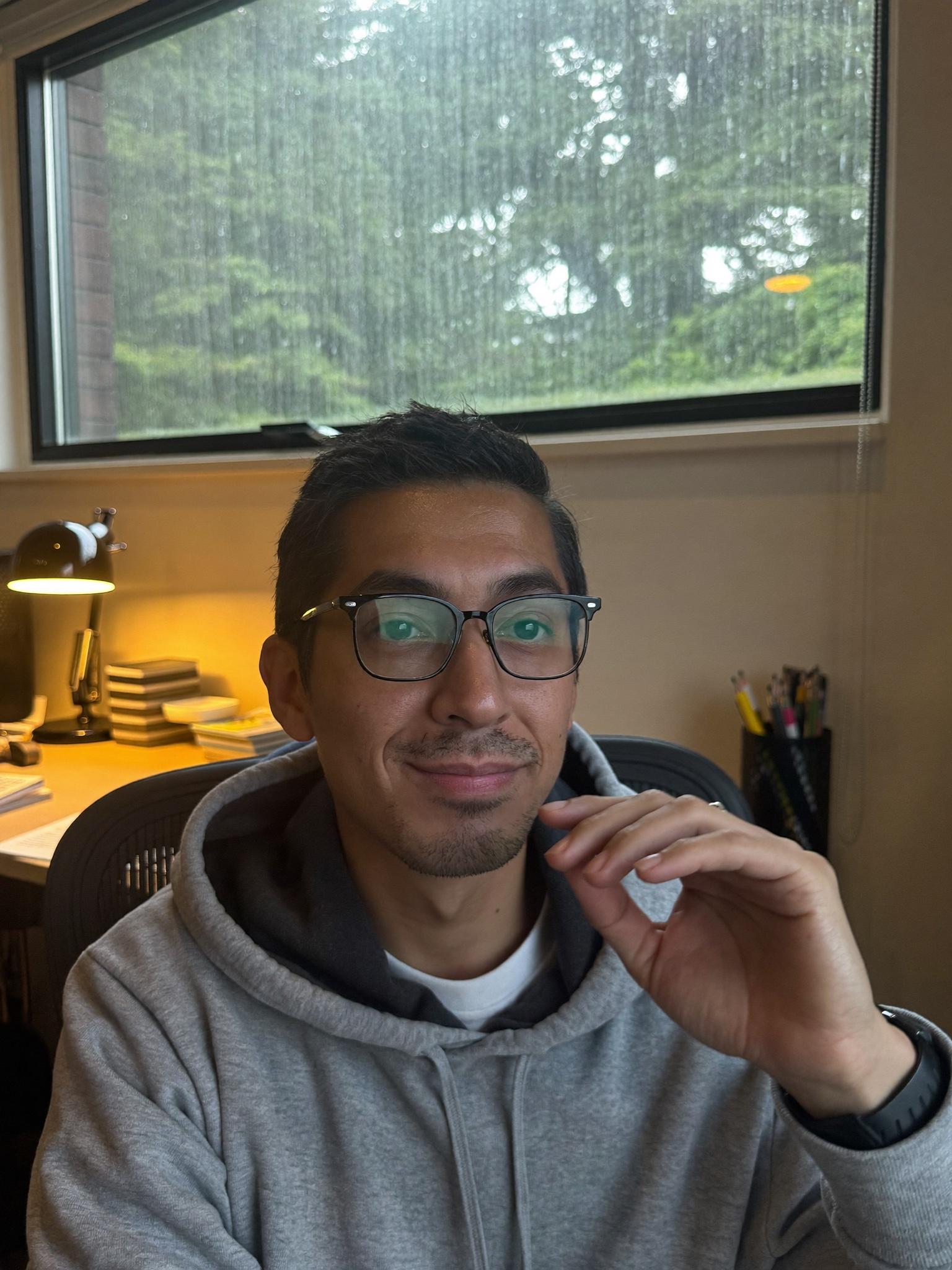 A man in his early forties at a home office desk near a rainy window in Seattle.